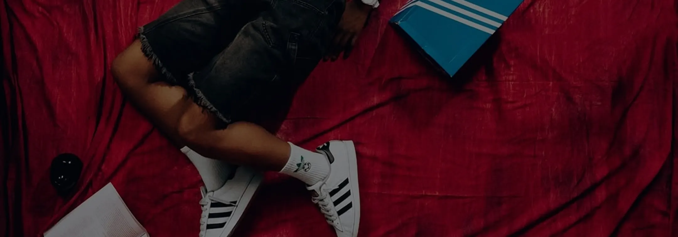 Person in black shorts and white Adidas shoes lying on a red surface with books nearby