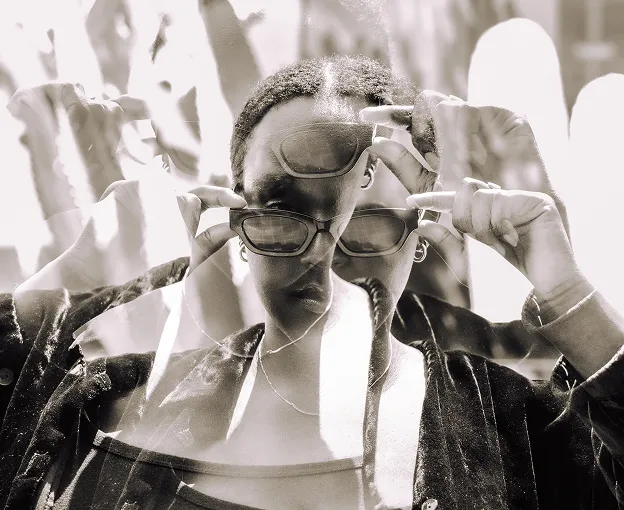 Black and white double exposure of a person adjusting sunglasses outdoors