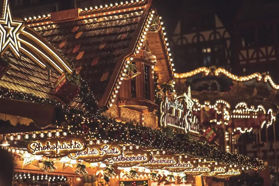 Beleuchtete Weihnachtsmarktbude mit Lichterketten und Karussell im Hintergrund