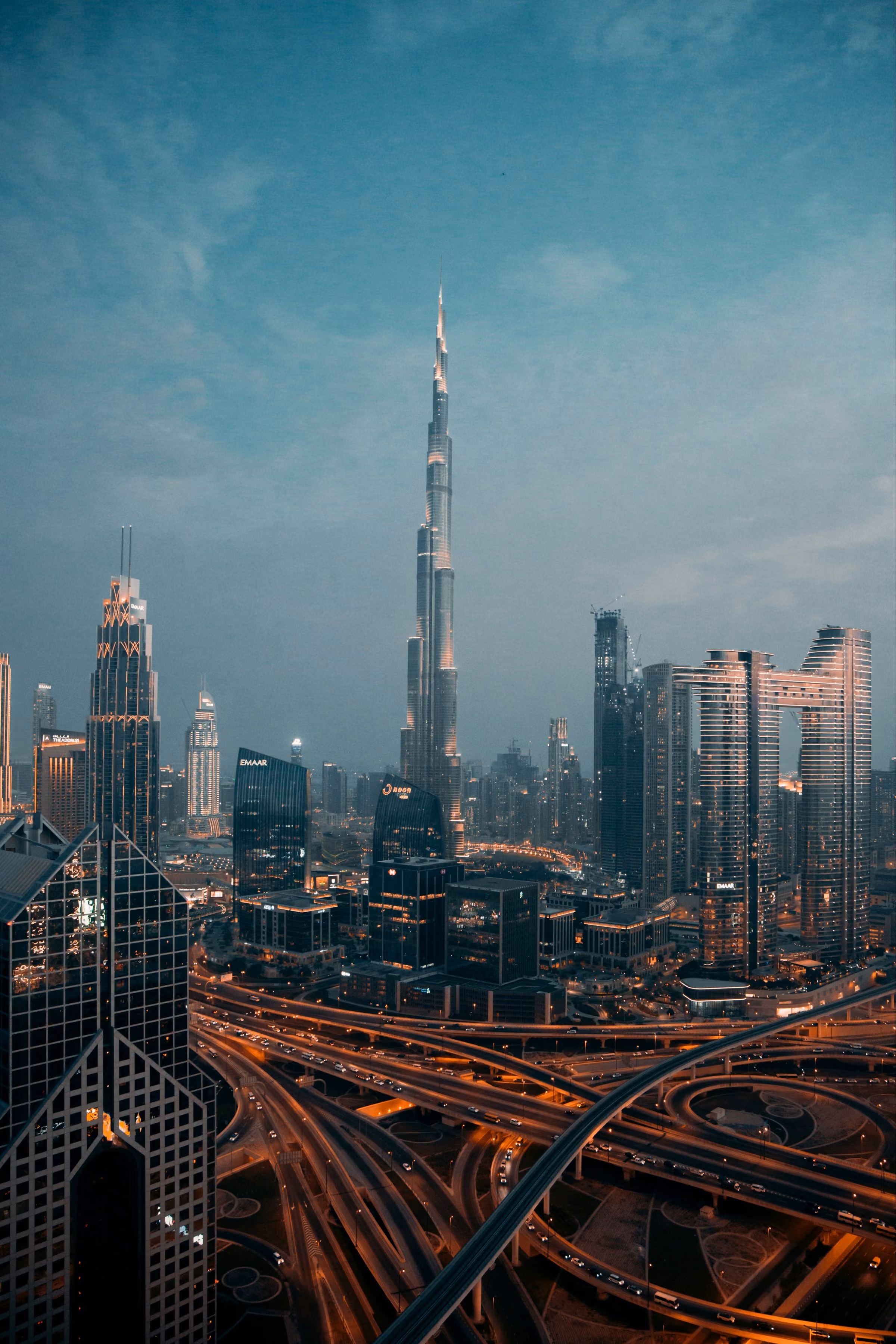 Night cityscape of Dubai with Burj Khalifa tower and lit highway interchange below.