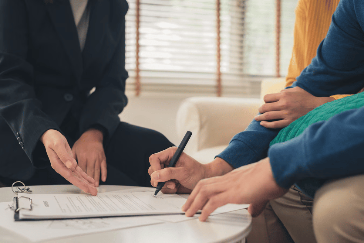 A person signing a contract with a person and a person sitting on a couch.