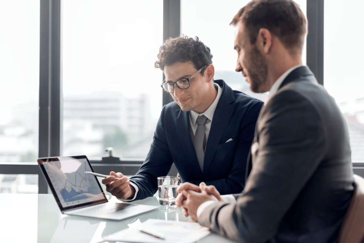 Two businessmen analyzing data on a tablet in a modern office setting.