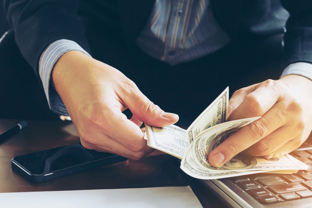 Close-up of hands holding cash with a calculator and notepad on a desk.