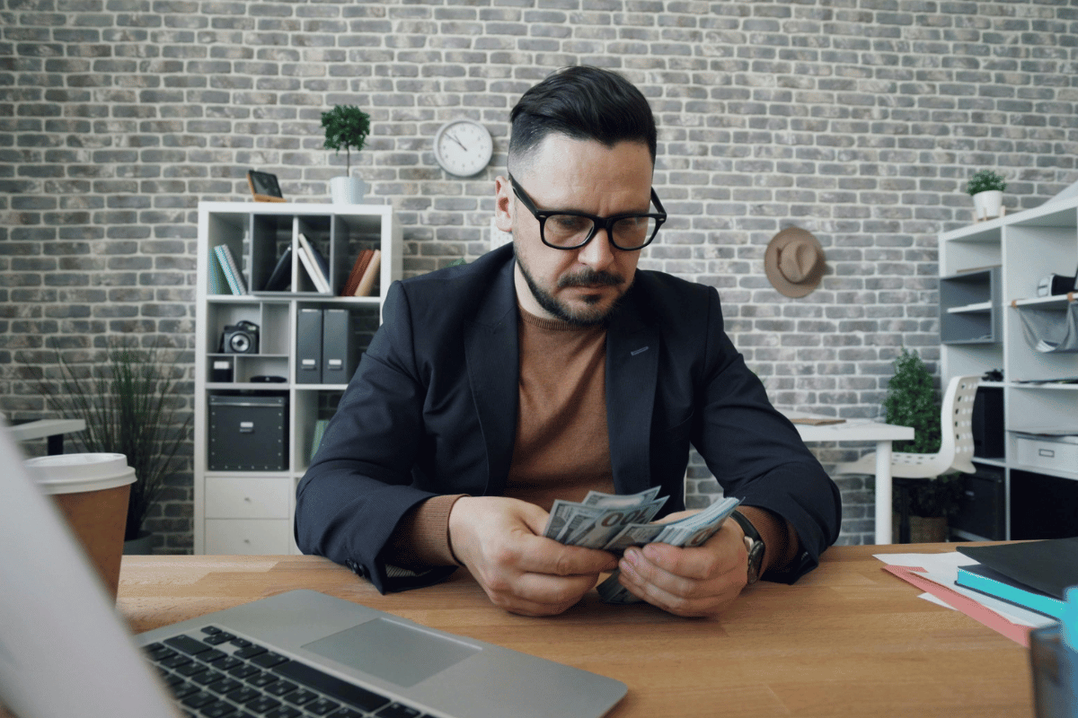 Businessman in glasses counting dollar bills at his desk.