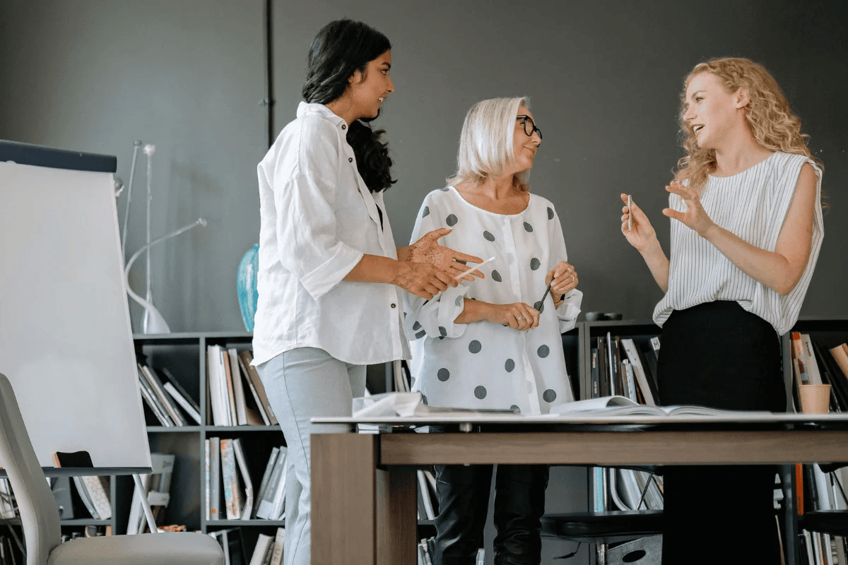 Three women colleagues having a discussion in a modern office.