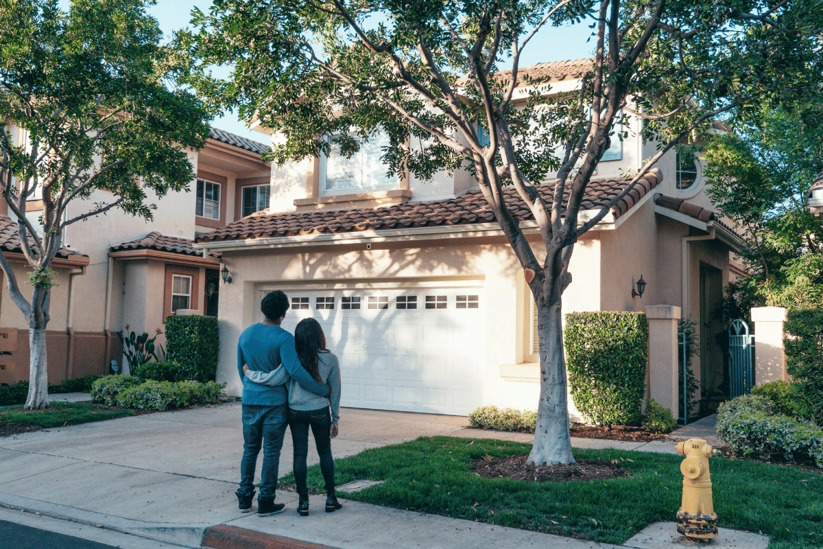 A couple standing in front of a suburban home with a clay tile roof and a garage.