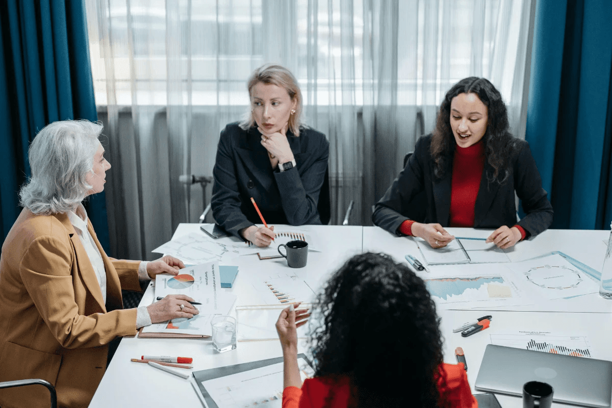 Four women discussing charts and graphs in a business meeting.