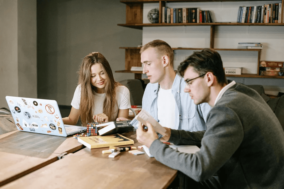 Three young professionals collaborating around a table with a laptop covered in stickers.