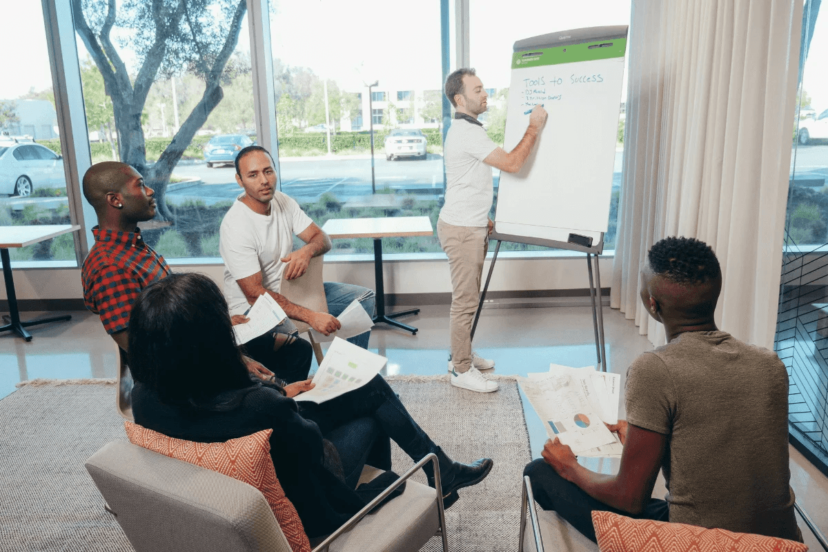 A diverse group of individuals sitting in a circle around a whiteboard, engaged in a discussion.