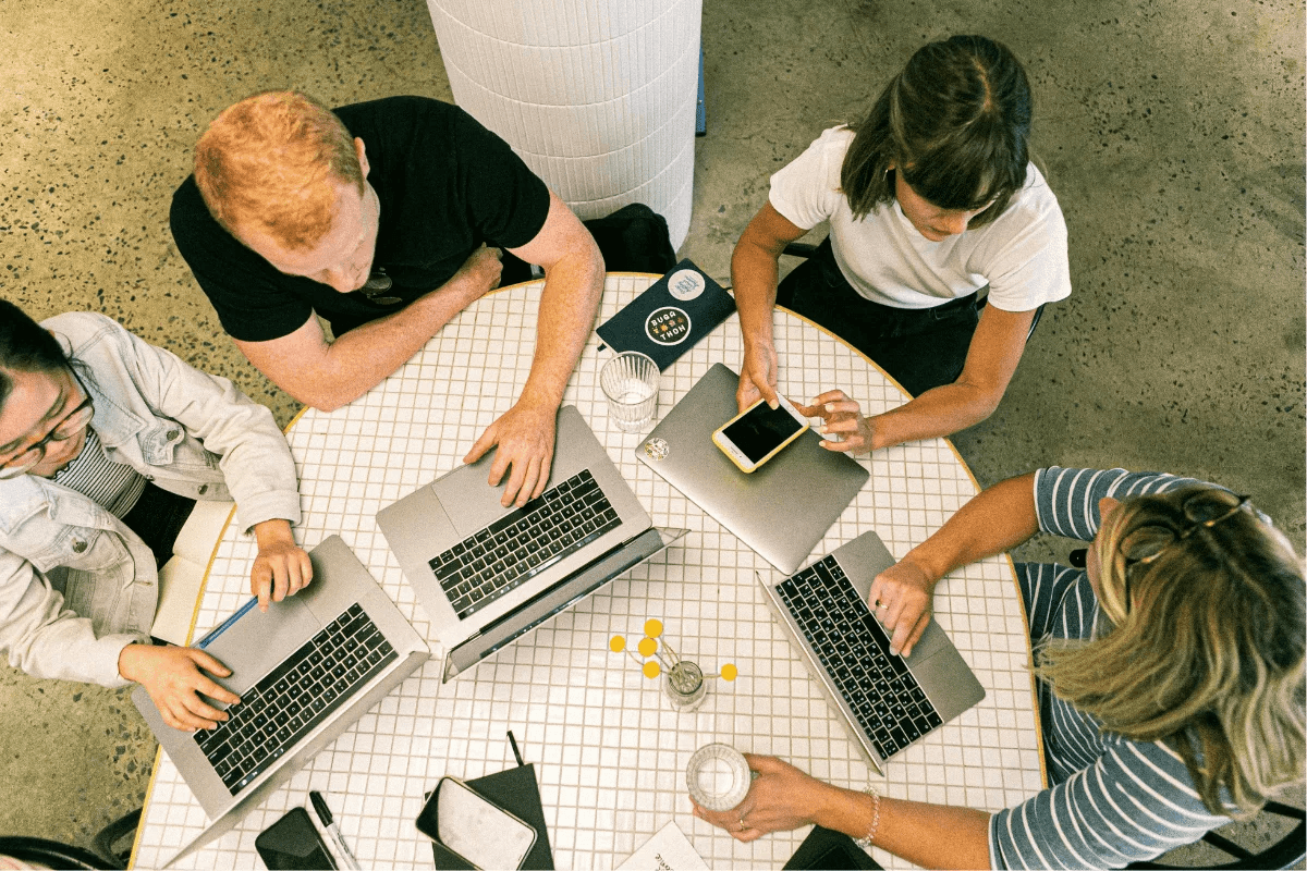 Overhead view of a team collaborating at a round table with laptops, notebooks, and a smartphone.