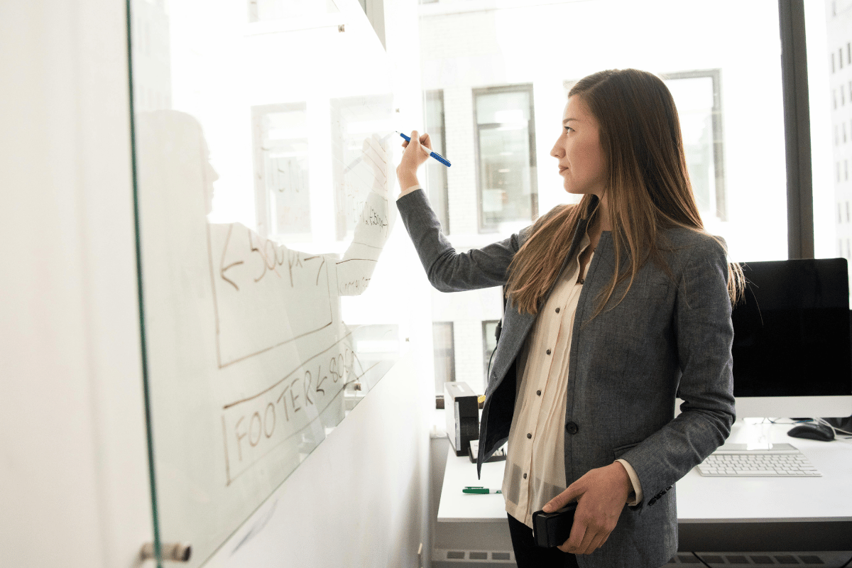 Professional woman writing on a whiteboard in a bright office, planning a project.