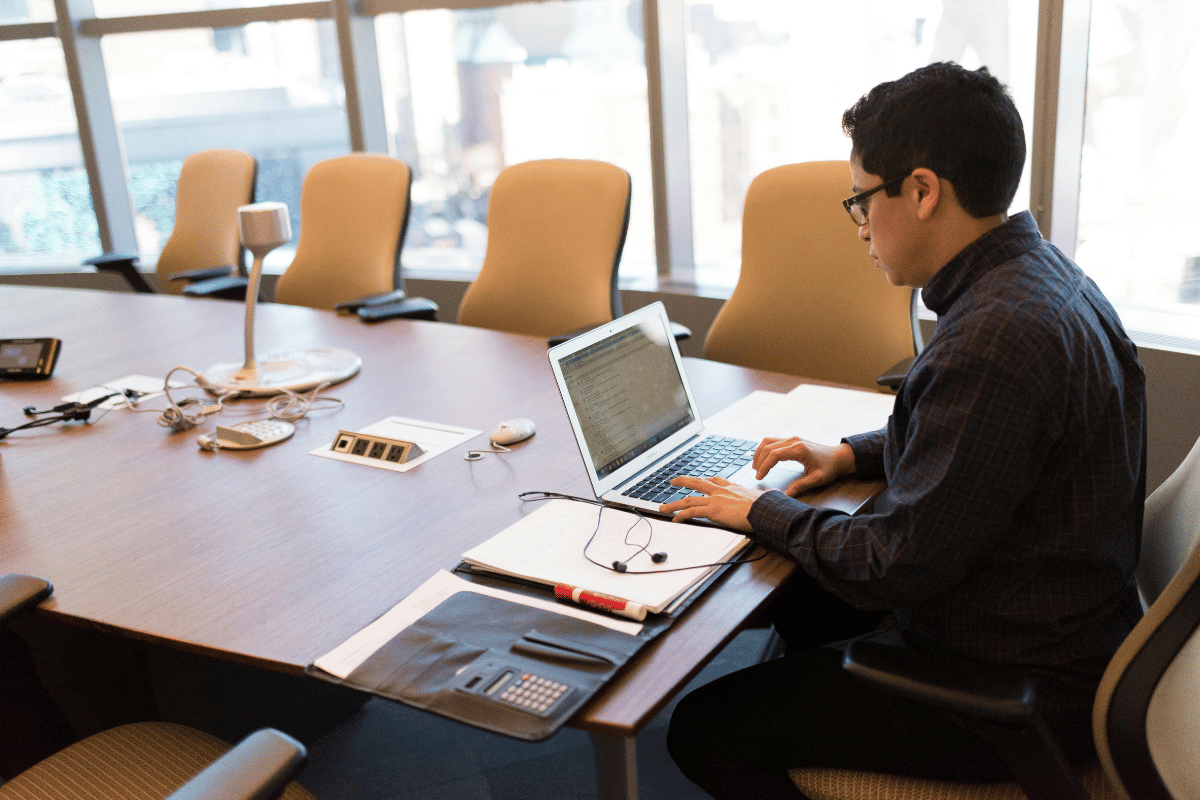 Young professional working on a laptop in a modern conference room with large windows.