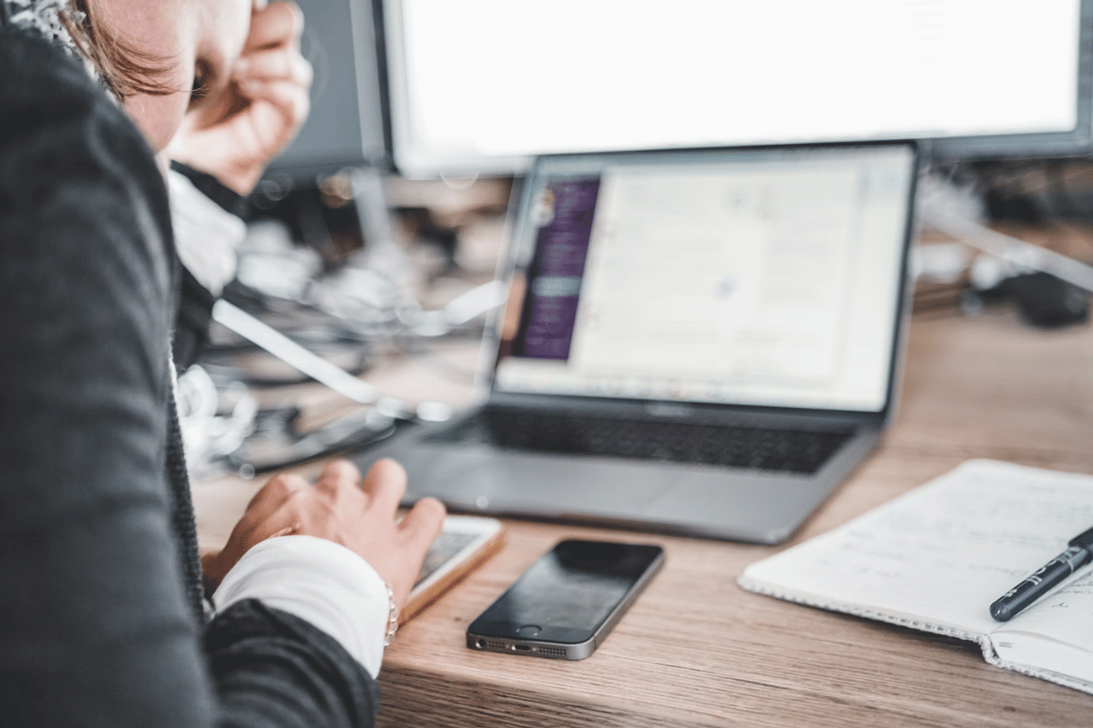 A businessperson working intently on a laptop with a smartphone and notepad on the desk.
