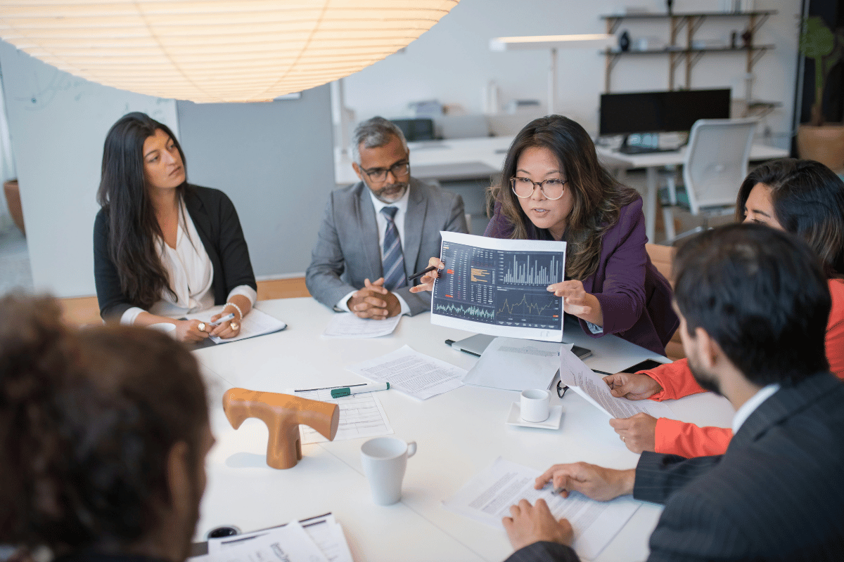 A diverse group of individuals gathered around a table, engaged in a discussion while examining a chart.