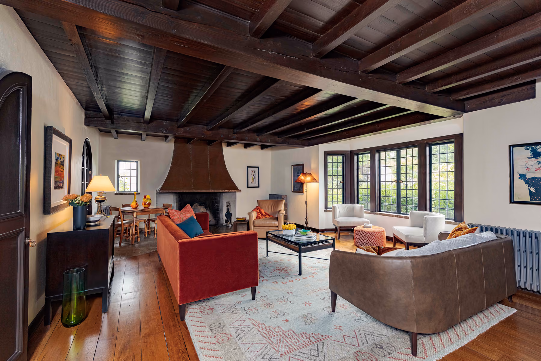 Spacious living room with wooden ceiling, fireplace, red and brown sofas, white chairs, and large windows.