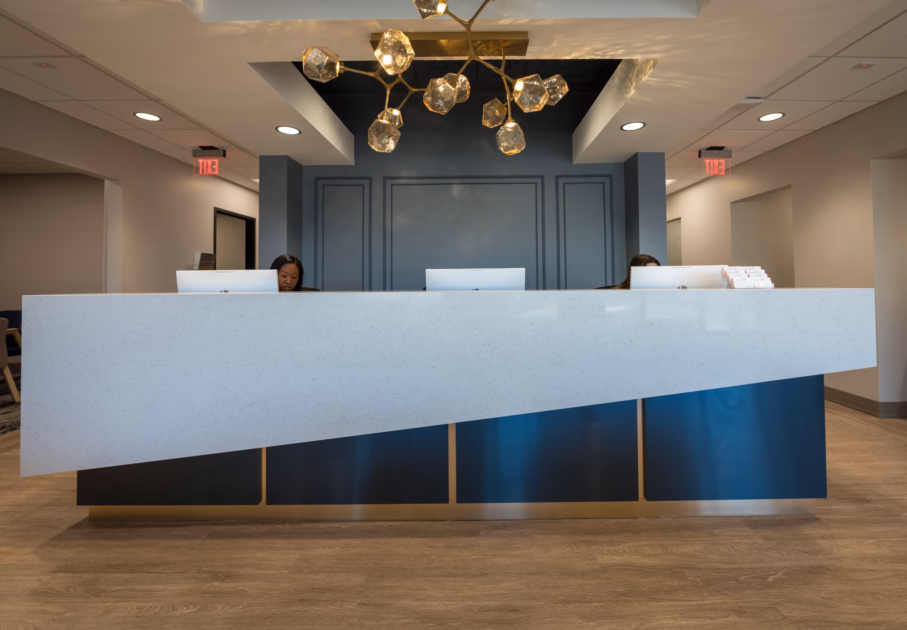 Modern reception desk with two staff working behind computers under a unique gold chandelier.
