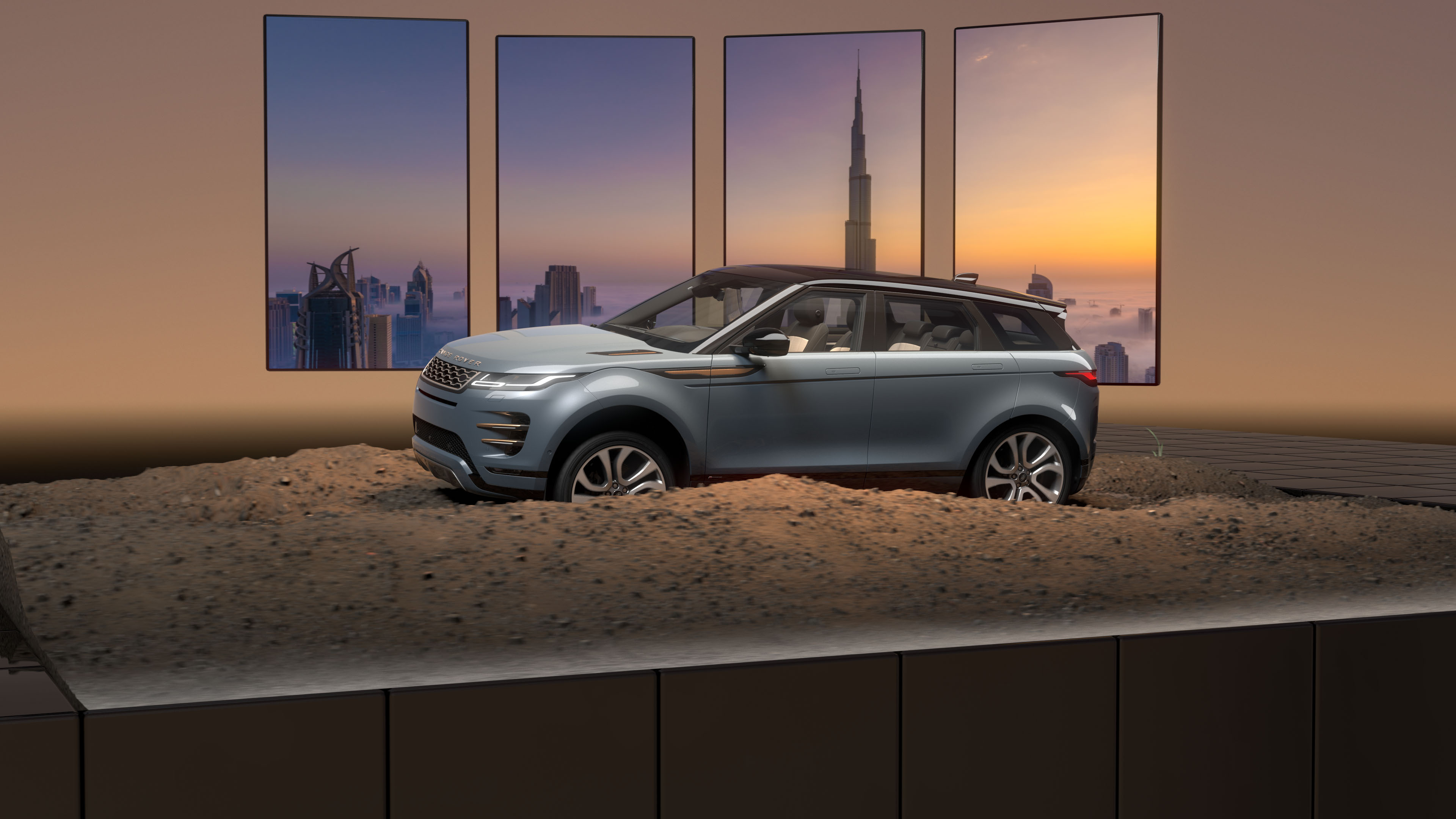 Silver Range Rover SUV displayed on dirt with Dubai skyline visible on four tall windows behind.