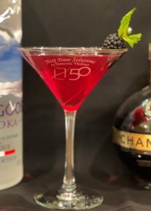 A red cocktail in a martini glass garnished with a blackberry