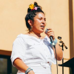 A young woman speaks into a microphone on stage