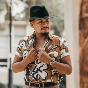 A young man in a hat and patterned shirt poses outdoors