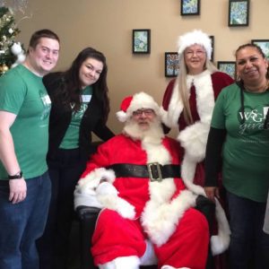 Volunteers in green shirts pose with Santa and Mrs. Claus