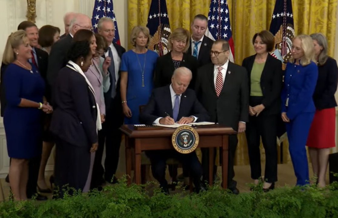 President Biden signs a bill at a White House ceremony surrounded by lawmakers