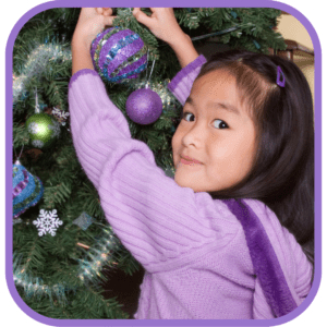 A young girl hangs an ornament on a holiday tree