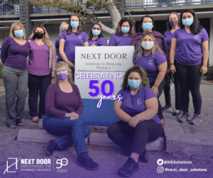 Next Door Solutions staff in purple shirts and masks celebrating 50 years