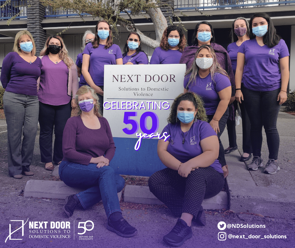 Next Door Solutions staff in purple shirts and masks celebrating 50 years