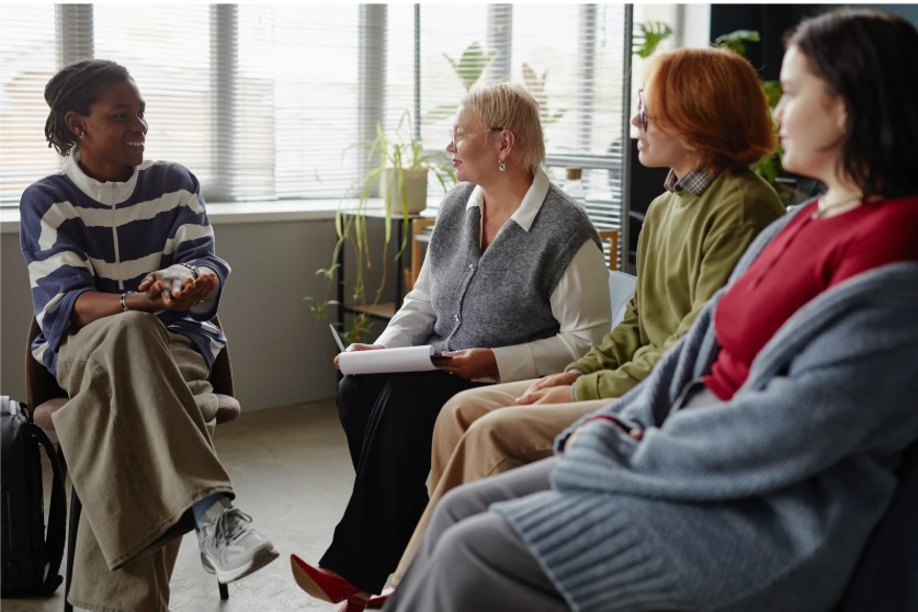 A group of women sit in a circle talking during a support group