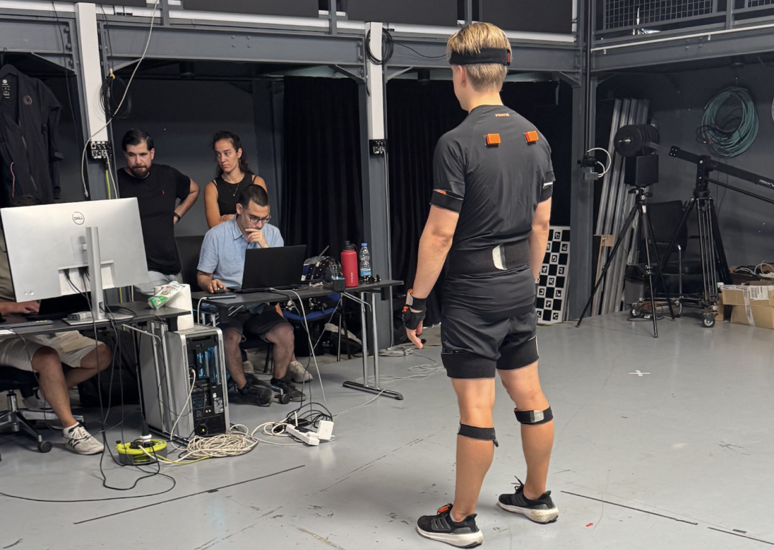 Researchers at recording workstations while a sensor-equipped athlete stands in the capture area