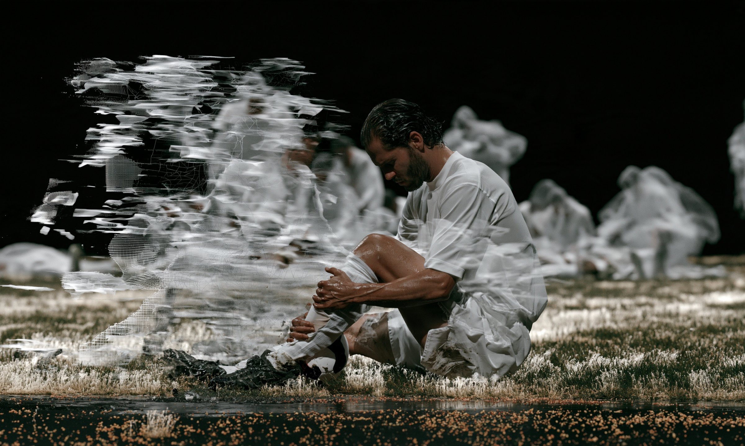 Athlete sitting on the pitch holding his ankle, with a point-cloud reconstruction dissolving around him