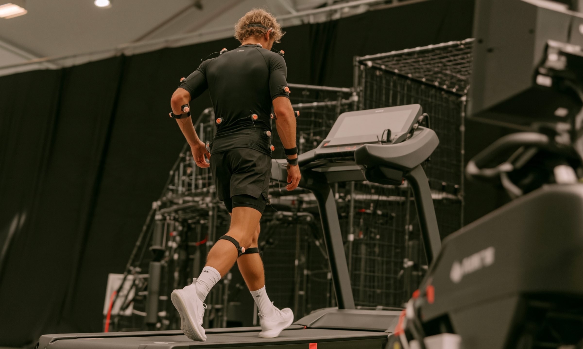 Athlete in a motion-capture suit with inertial sensors walking on a treadmill in a lab