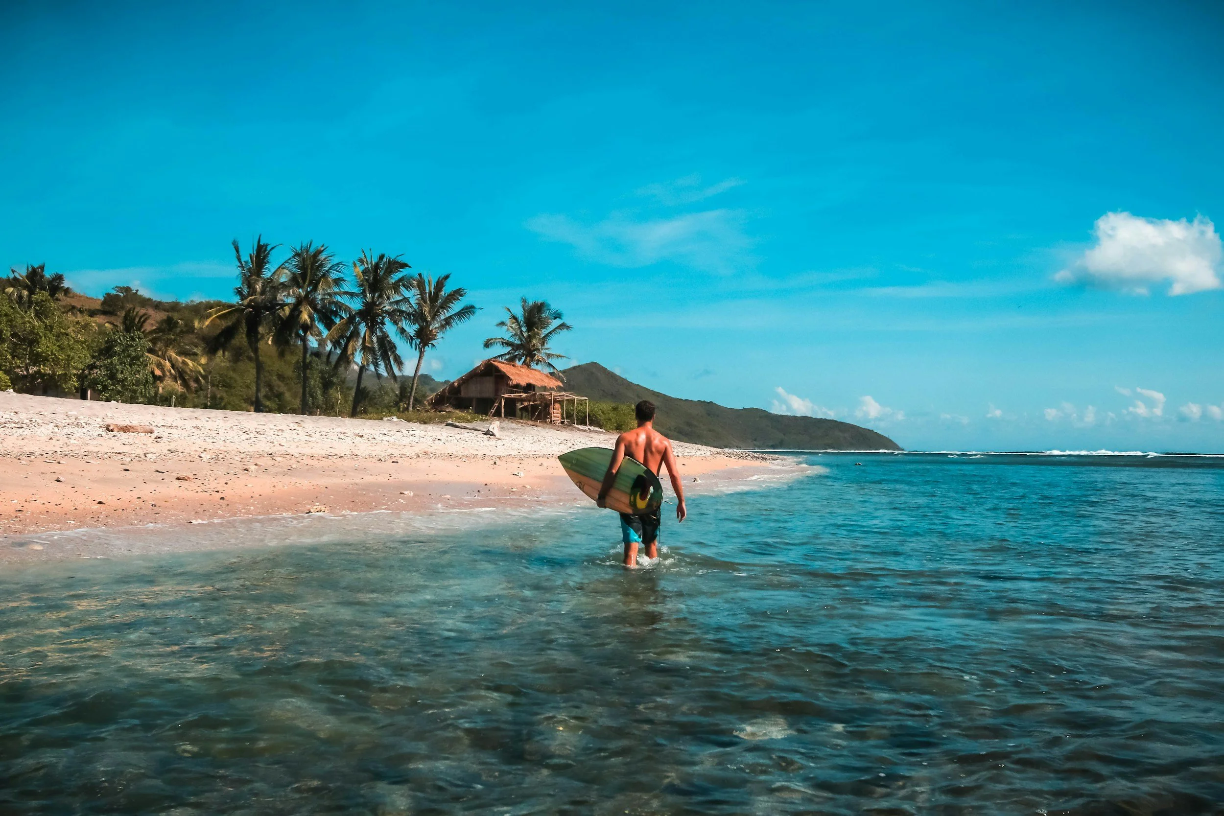 Surfer walking into the ocean with board at Kuta Lombok beach