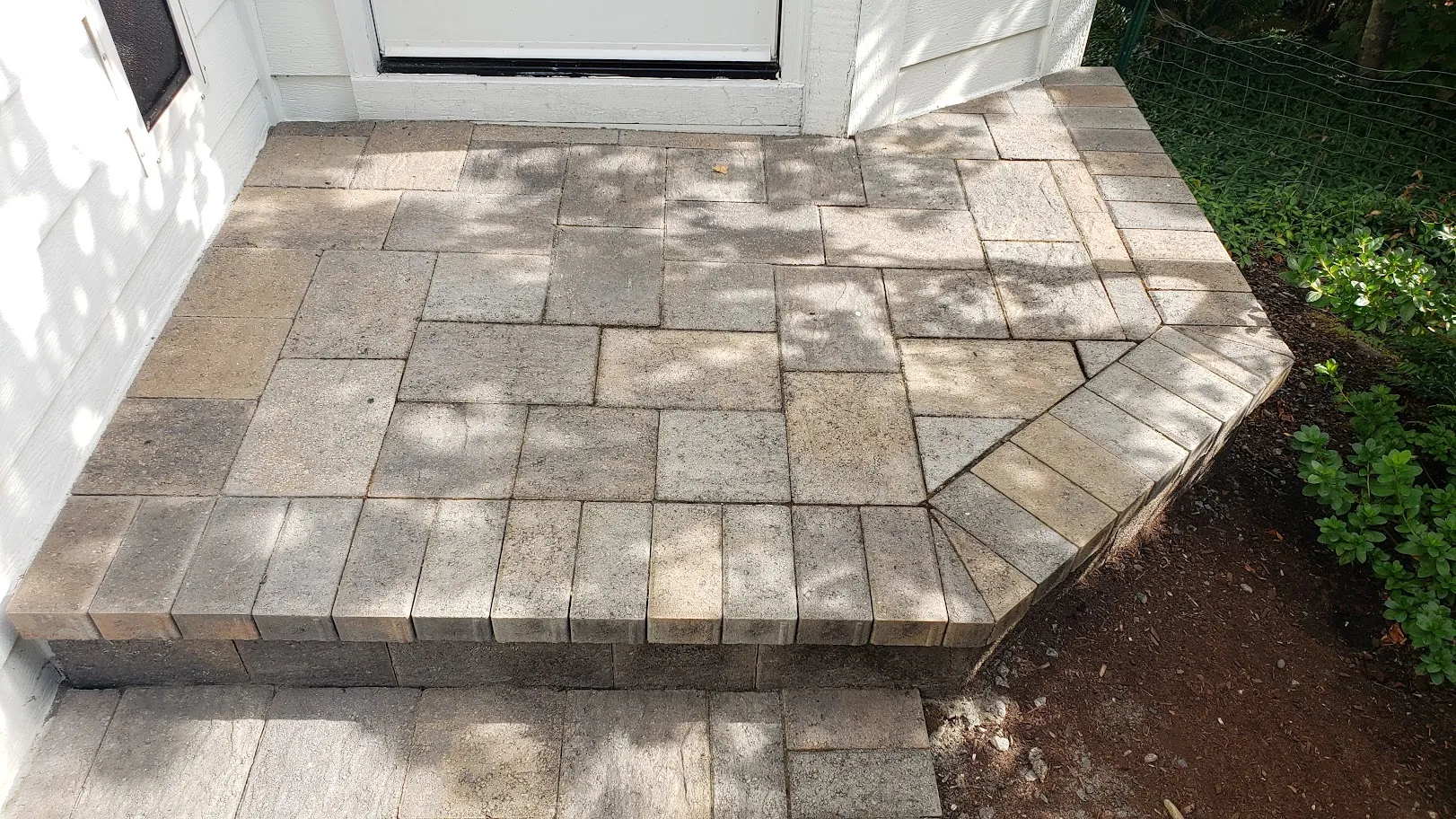 A paver entry step and landing before restoration, the stone darkened by soiling and organic growth