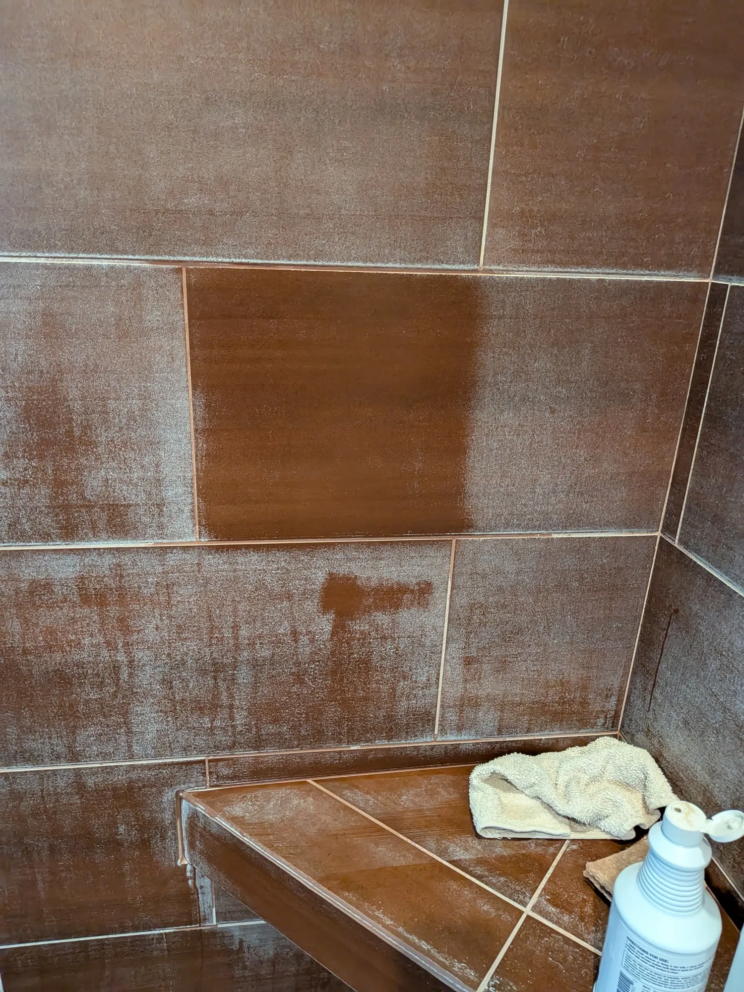 The same shower wall part way through cleaning, with one panel cleared to deep brown tile beside panels still white with mineral film