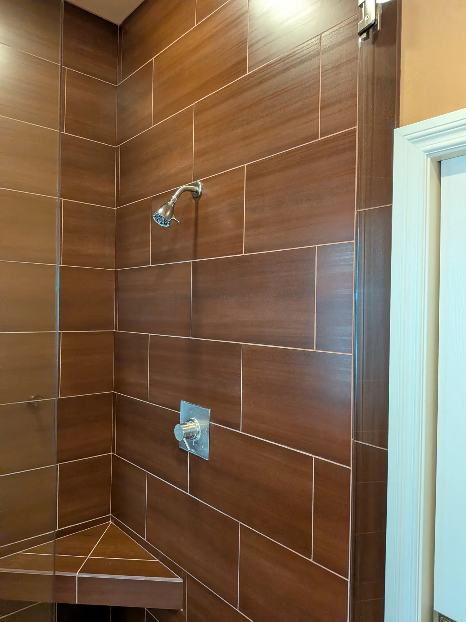 The restored shower valve and showerhead wall, brown tile clean and grout lines uniform