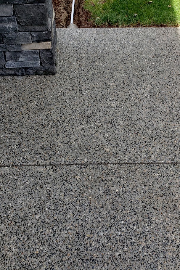 A cleaned exposed aggregate walkway running beside a stacked stone column and lawn