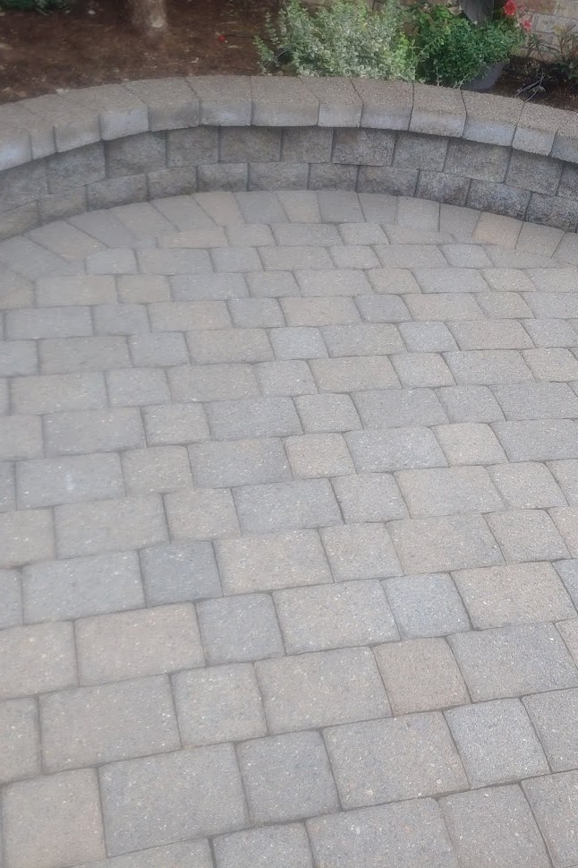 A restored paver patio behind a curved stacked seat wall in a back garden