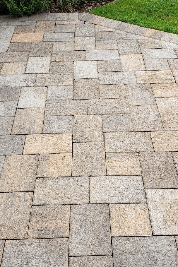 A cleaned paver patio in warm tan and grey stone meeting a trimmed lawn edge