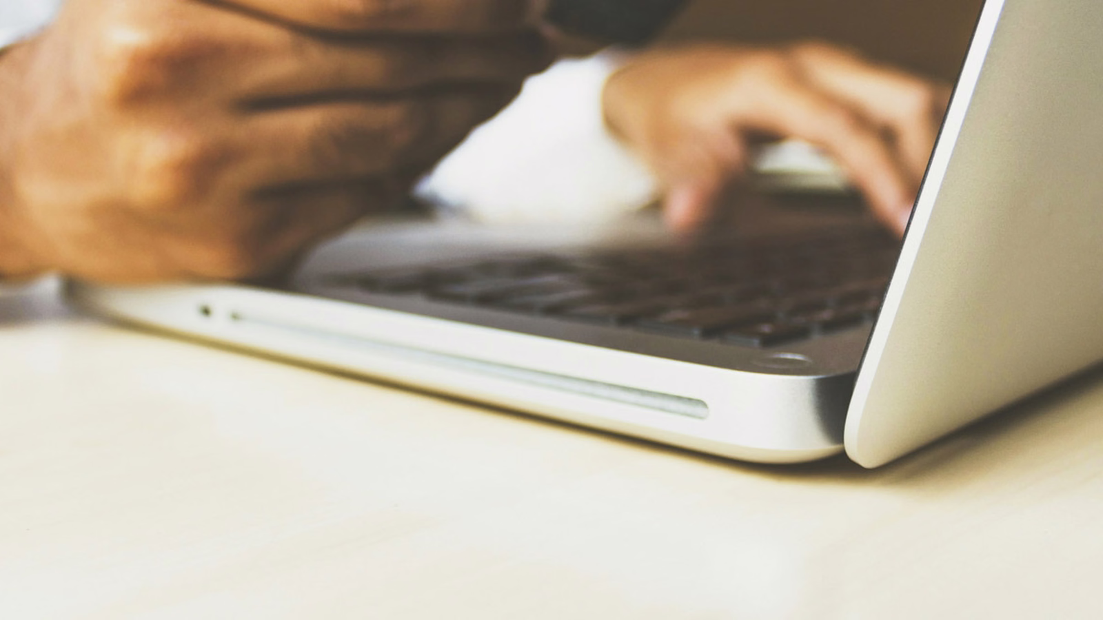 Hands typing on a laptop keyboard at a desk