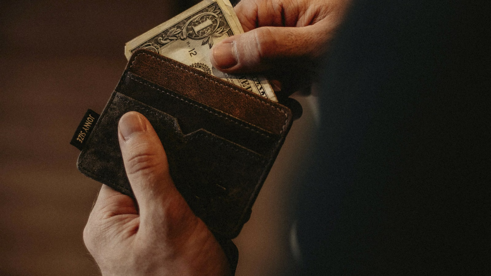 Hand pulling a dollar bill out of a leather wallet