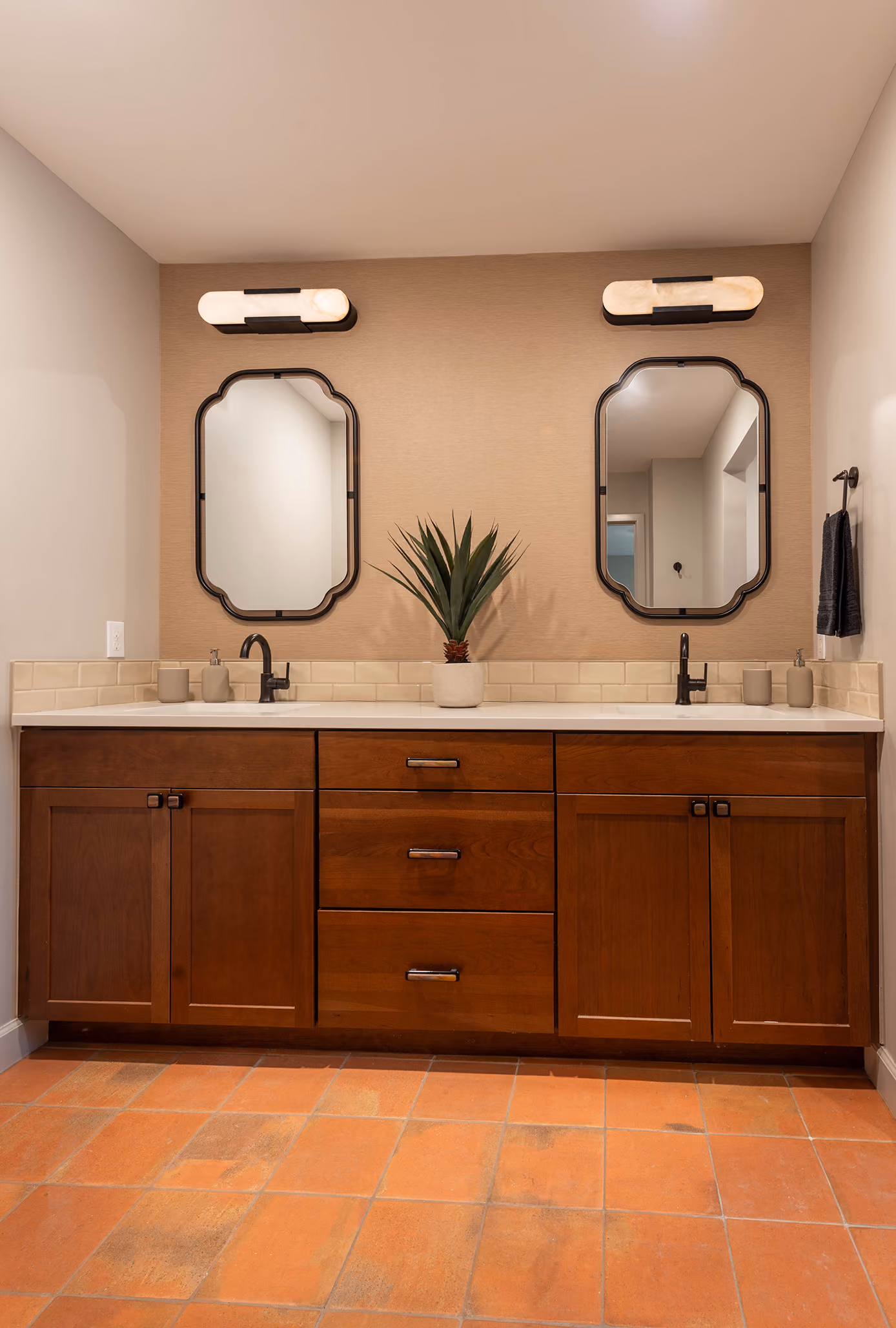 Wide view of a dark teal double-sink bathroom vanity with arched mirrors and terracotta tile floor