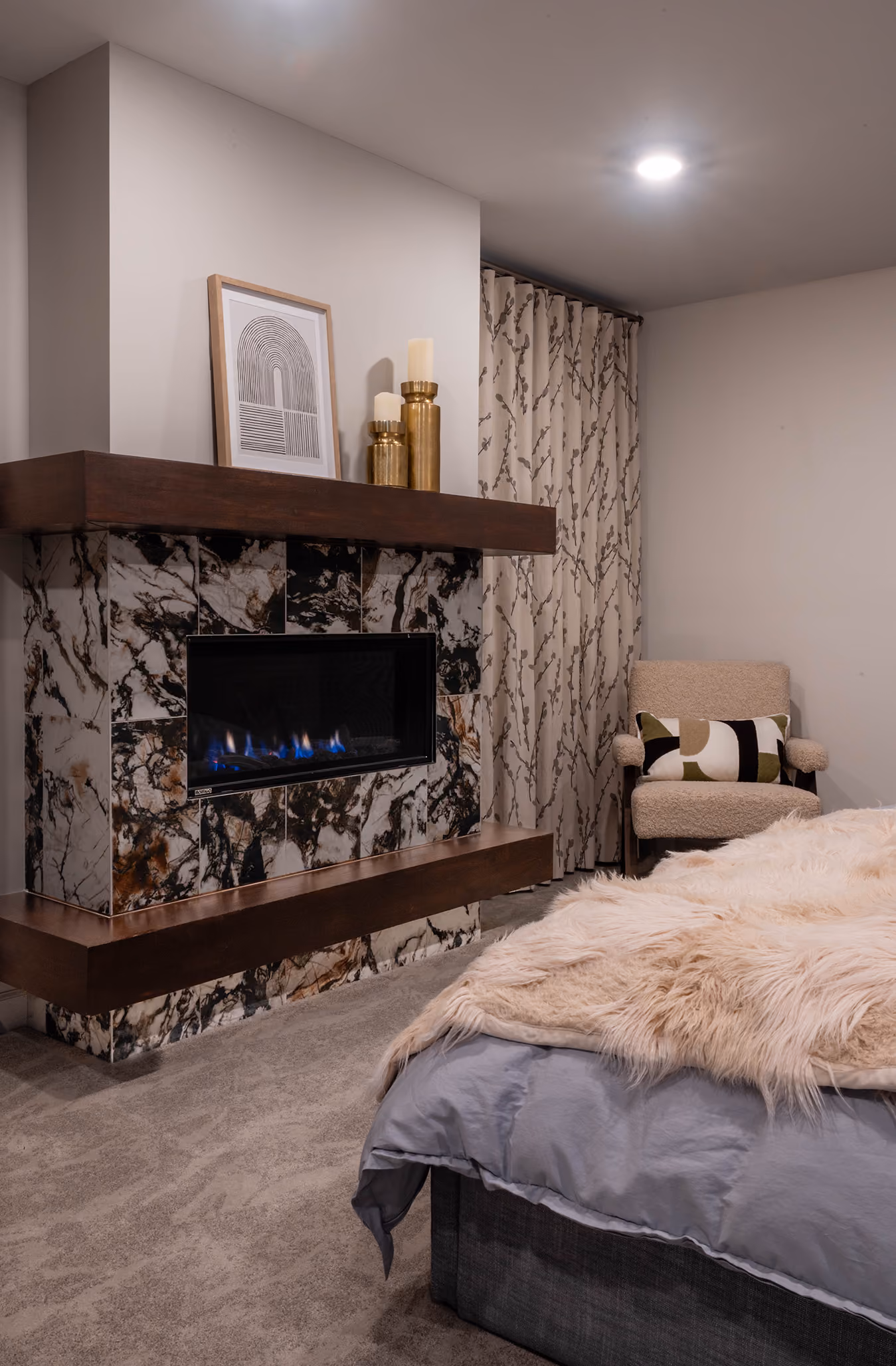 Bedroom with a linear gas fireplace framed in stone slab and a faux-fur throw on the bed