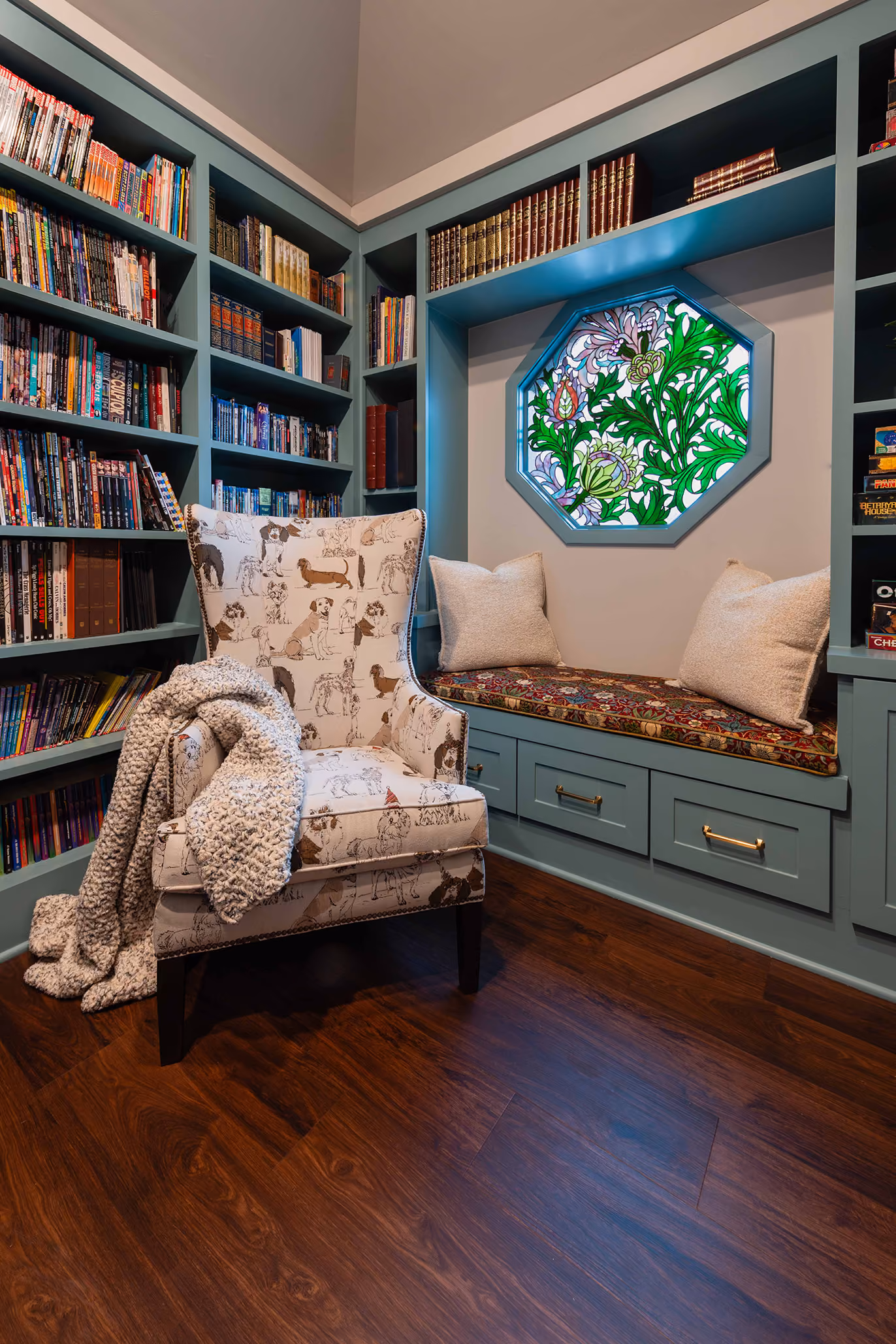 Home library nook with a custom dog-print wingback armchair, built-in bookshelves, and a stained-glass window seat