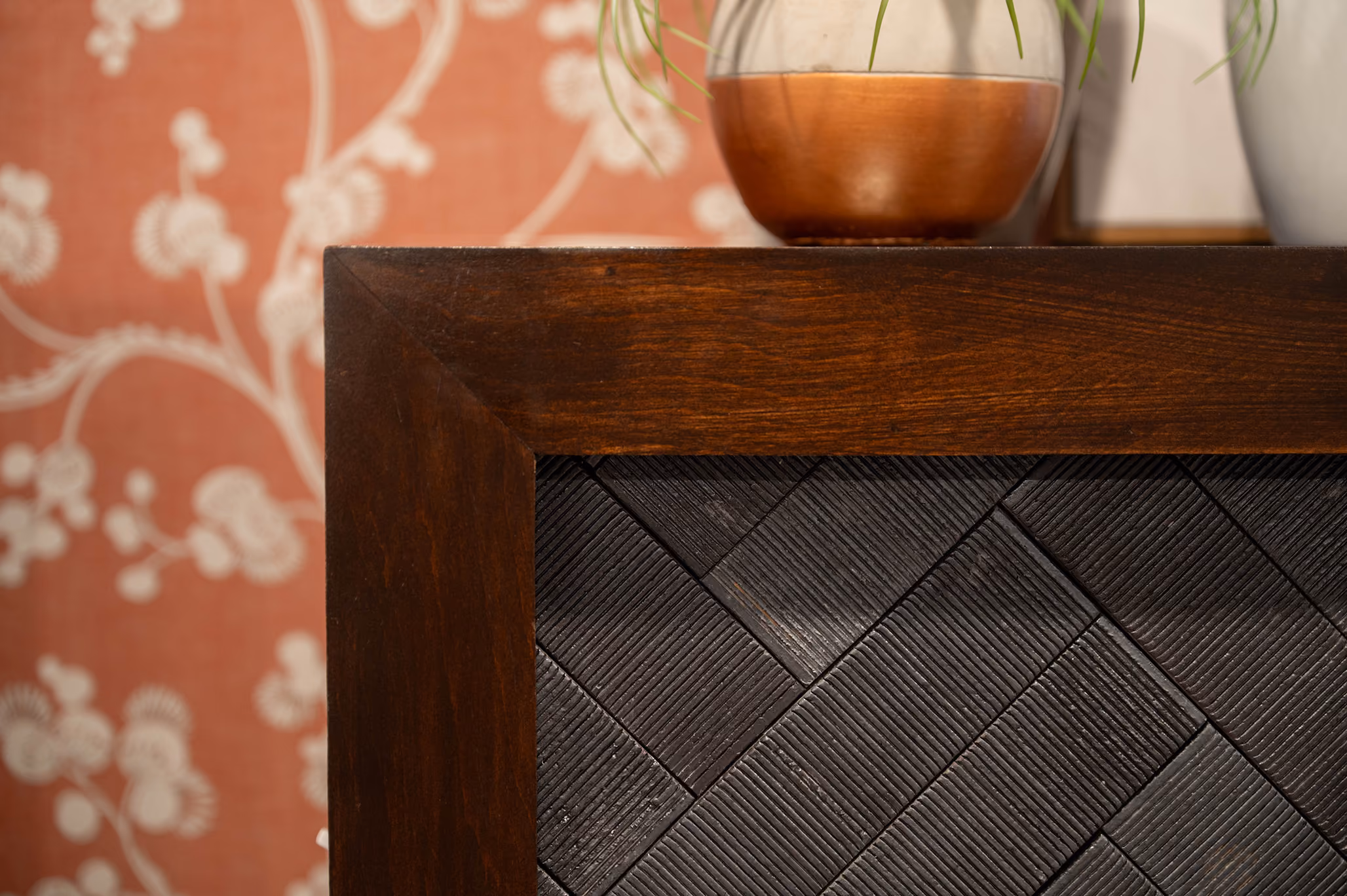 Close-up of a fireplace mantel corner with dark herringbone tile and floral wallpaper