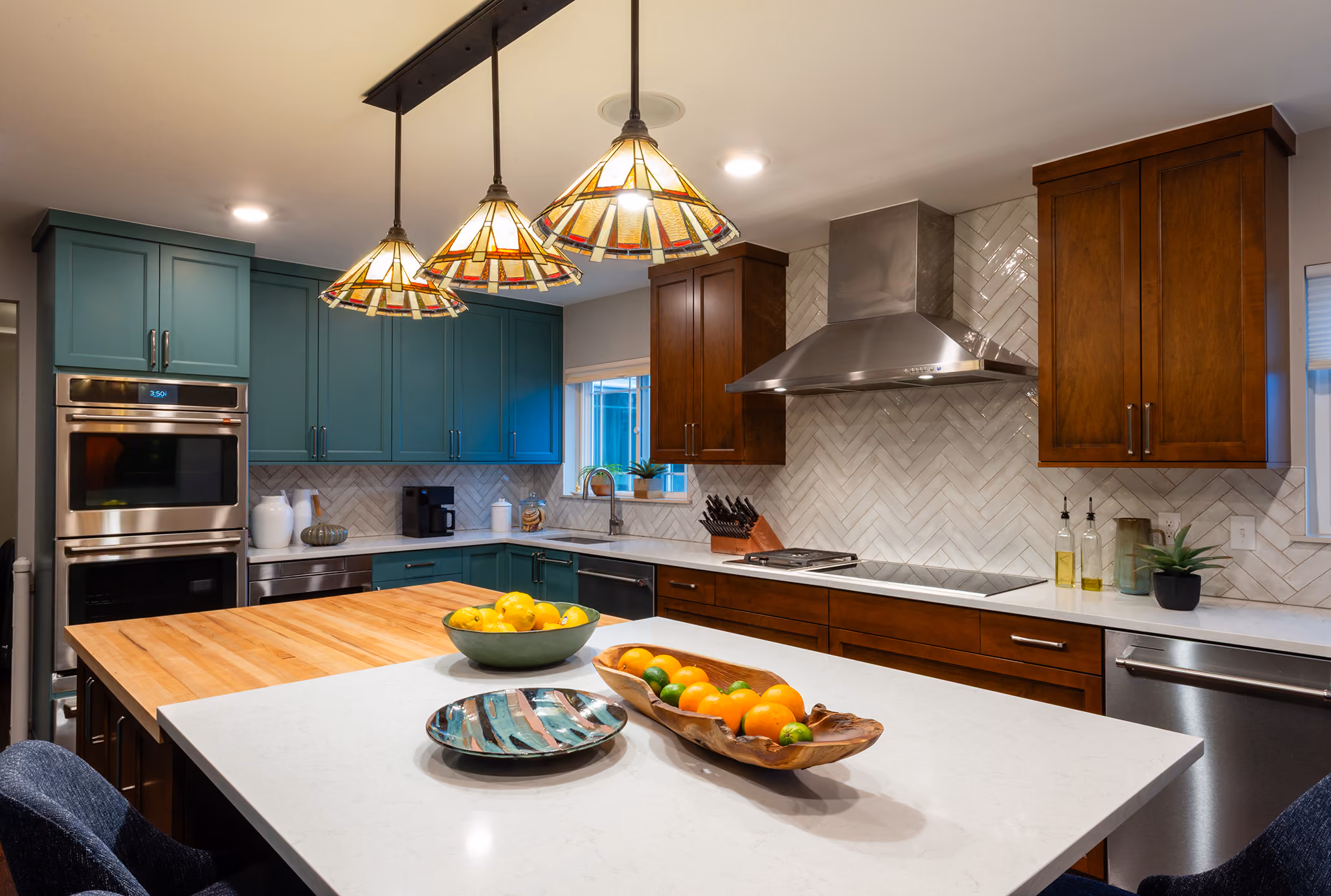 Kitchen with teal and stained-wood cabinetry, herringbone tile backsplash, and Arts and Crafts-style stained glass pendant lights over the island
