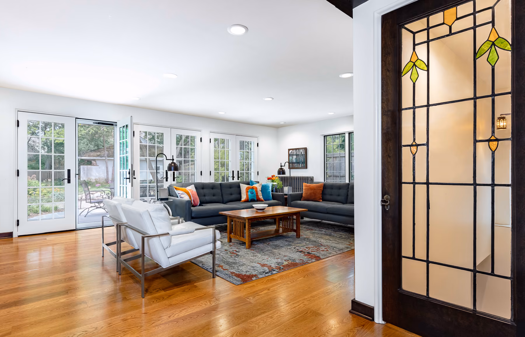 Family room with a charcoal tufted sectional, French doors to the backyard, and an original stained-glass door in a historic Birmingham, Michigan renovation