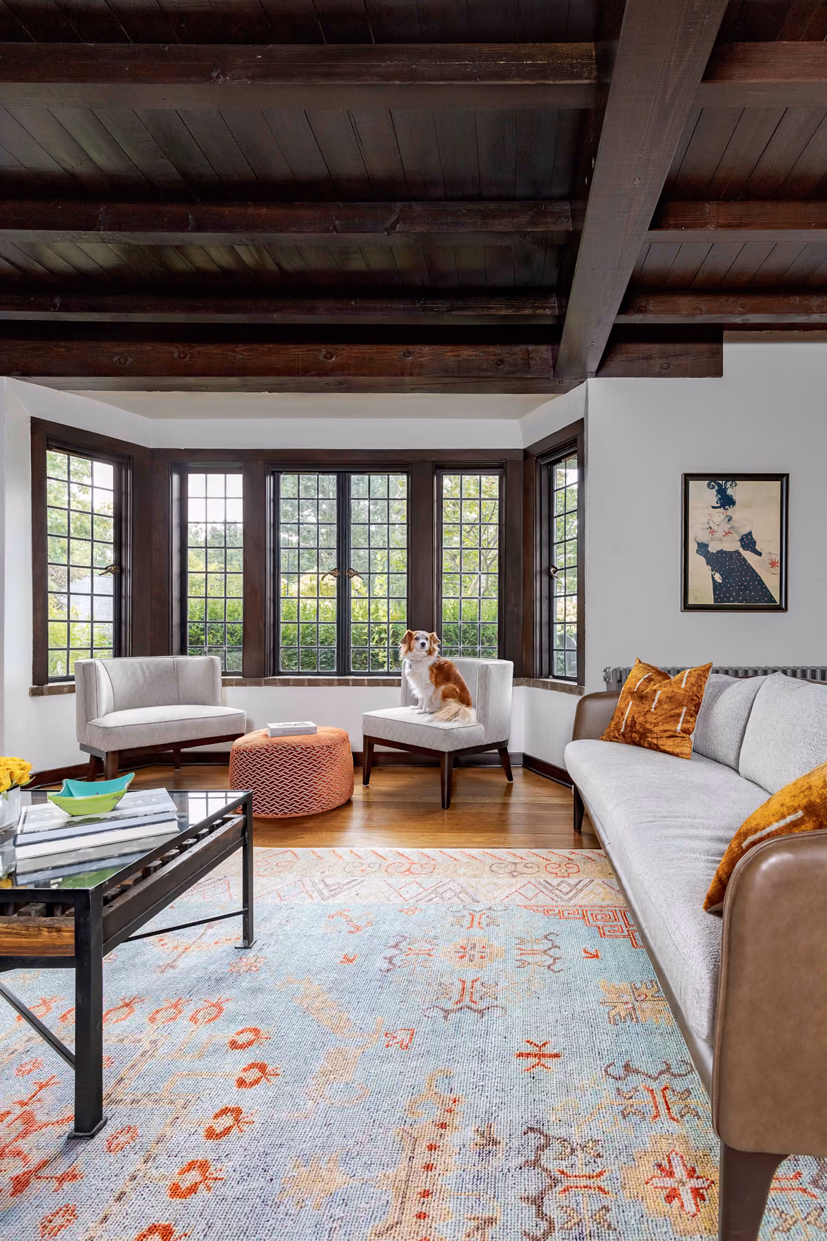 Living room bay window with leaded glass panes, exposed wood beam ceiling, and a vintage-style area rug