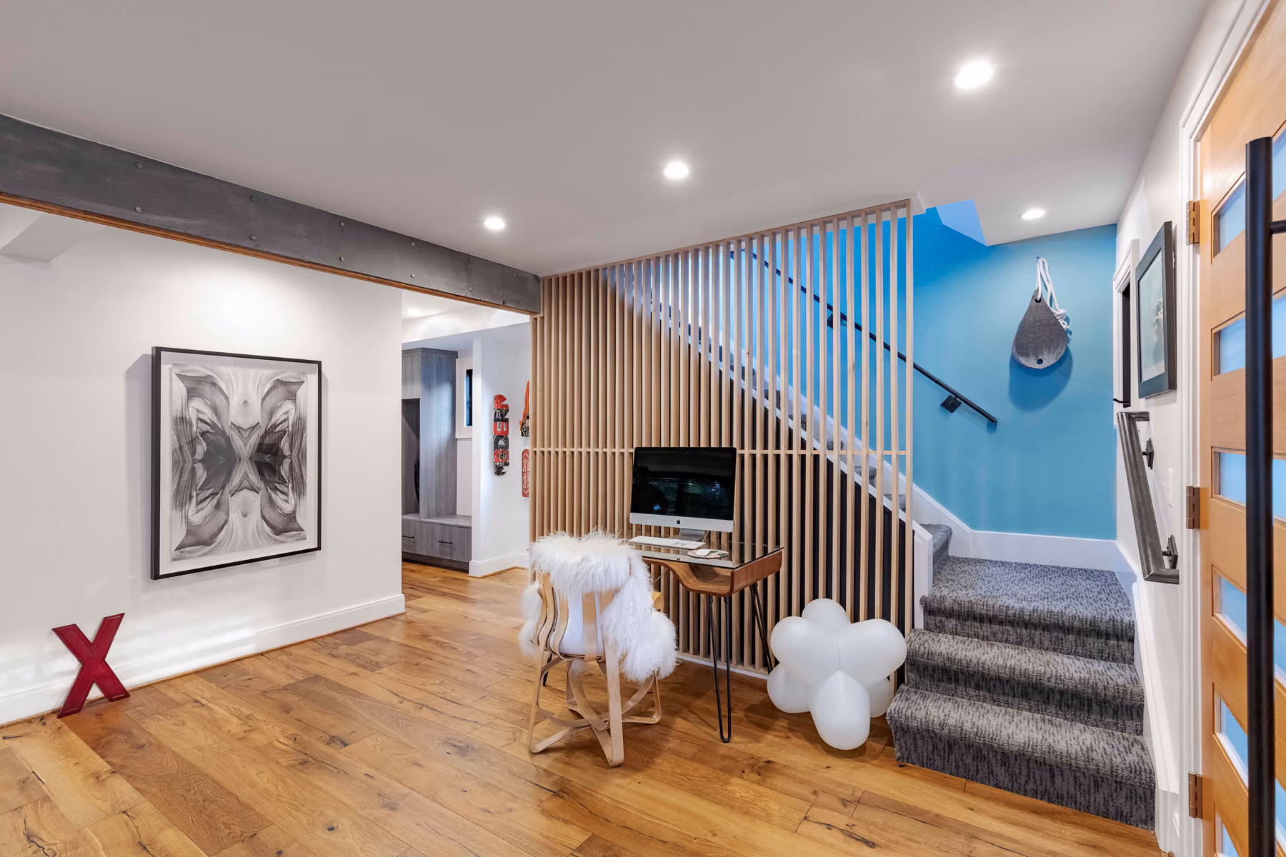 Open-plan living area with a wood-slat stair screen, blue accent wall, and gallery wall of curated art
